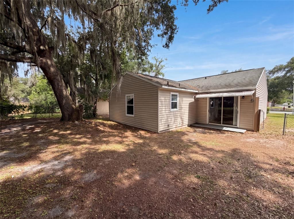 The exterior of a tan, single-story house features vinyl siding and a large oak tree — 2715 LORRAINE DRIVE, LEESBURG, FL