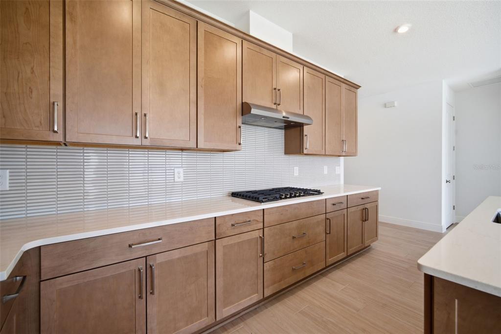 A kitchen features light wood cabinets, white countertops, a tiled backsplash, and stainless steel appliances — 7629 MARINA BAY COVE, PALMETTO, FL