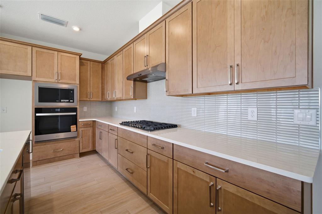 A kitchen features light wood cabinets, a gas cooktop, stainless steel appliances, and tiled backsplash — 7629 MARINA BAY COVE, PALMETTO, FL