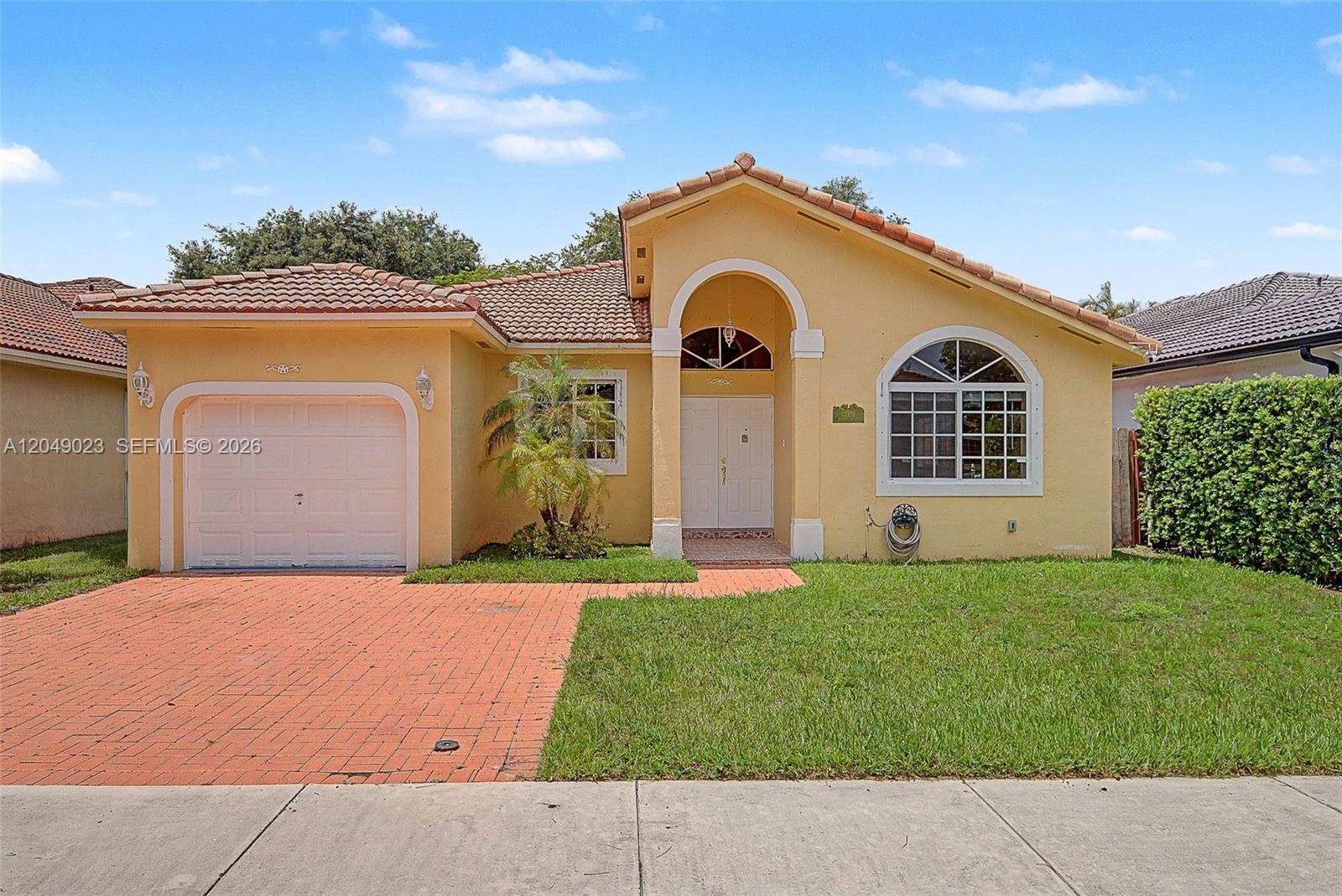 A single-story yellow house features a tiled roof, arched entryway, and a brick driveway — 15339 SW 32 TER # 0, Miami FL 33185, MIAMI, FL