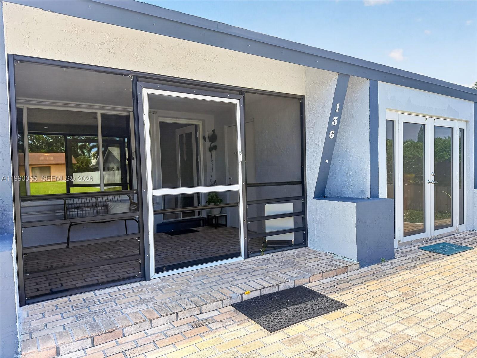 A screened-in porch with a brick patio sits beside a house entrance with glass doors — 136 SE 2nd Ct, Dania Beach FL 33004, DANIA BEACH, FL