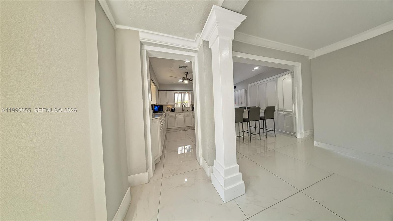 A view through a columned doorway into a white kitchen with tile flooring — 136 SE 2nd Ct, Dania Beach FL 33004, DANIA BEACH, FL