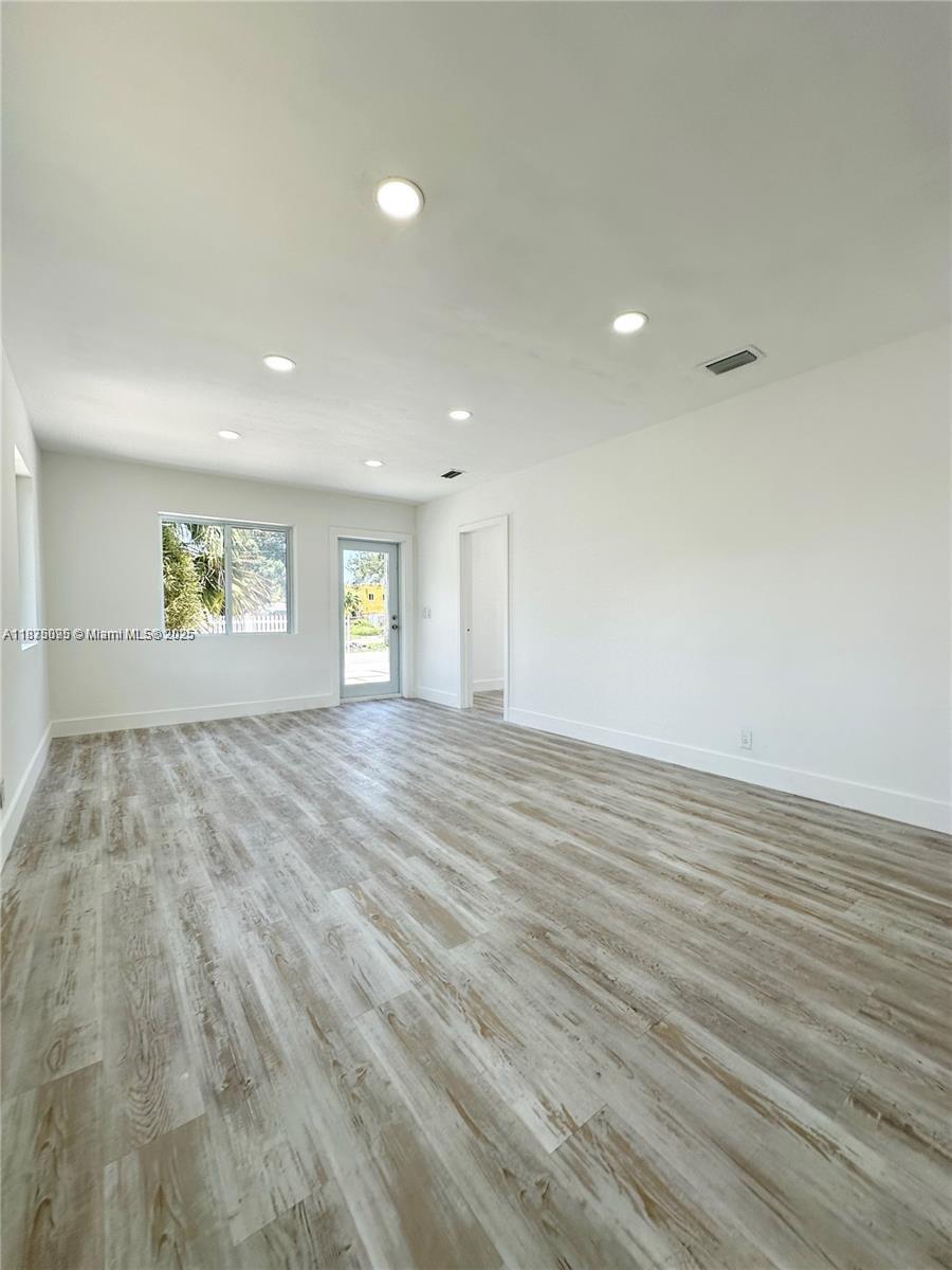 An empty room features light wood-look flooring, white walls, recessed lighting, and a glass door — 2740 NW 49th St, Miami FL 33142, MIAMI, FL