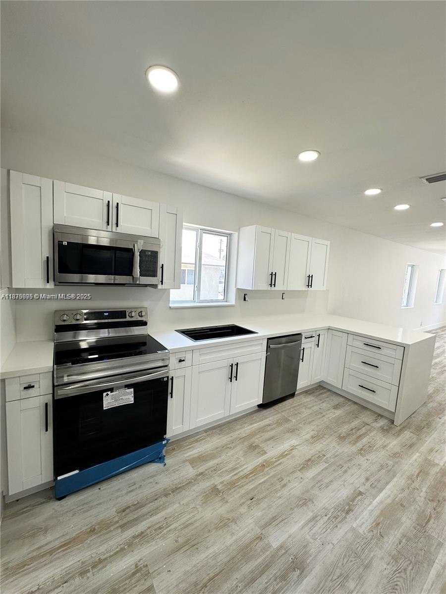 A modern kitchen features white shaker cabinets, stainless steel appliances, and light wood-look flooring — 2740 NW 49th St, Miami FL 33142, MIAMI, FL