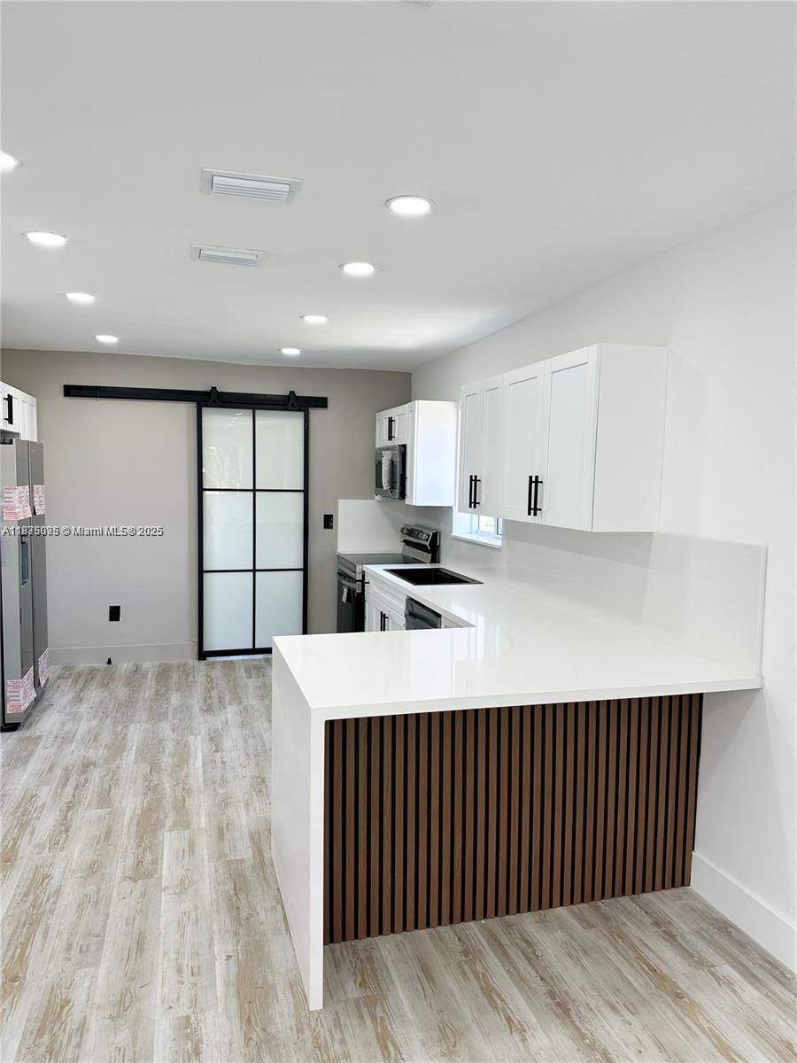 A modern kitchen features white cabinetry, a white quartz peninsula with wood slats, and flooring — 2740 NW 49th St, Miami FL 33142, MIAMI, FL