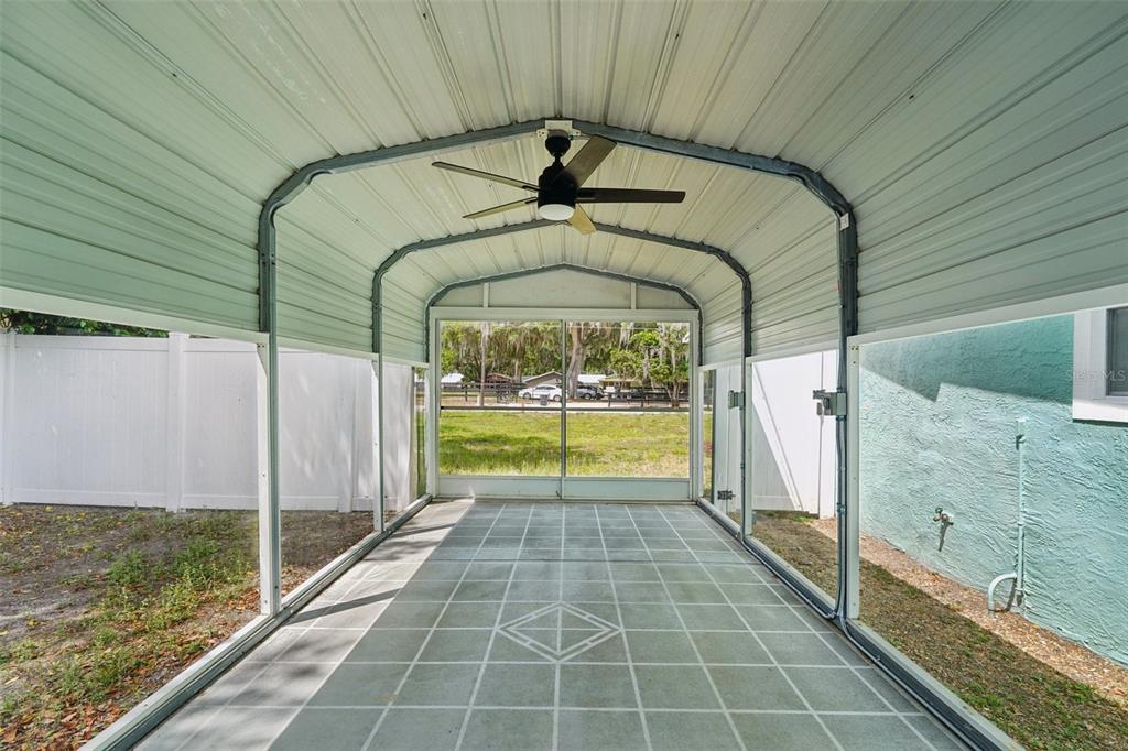 A screened-in carport with a metal roof, ceiling fan, and painted concrete flooring — 12385 SE 135TH COURT, OCKLAWAHA, FL