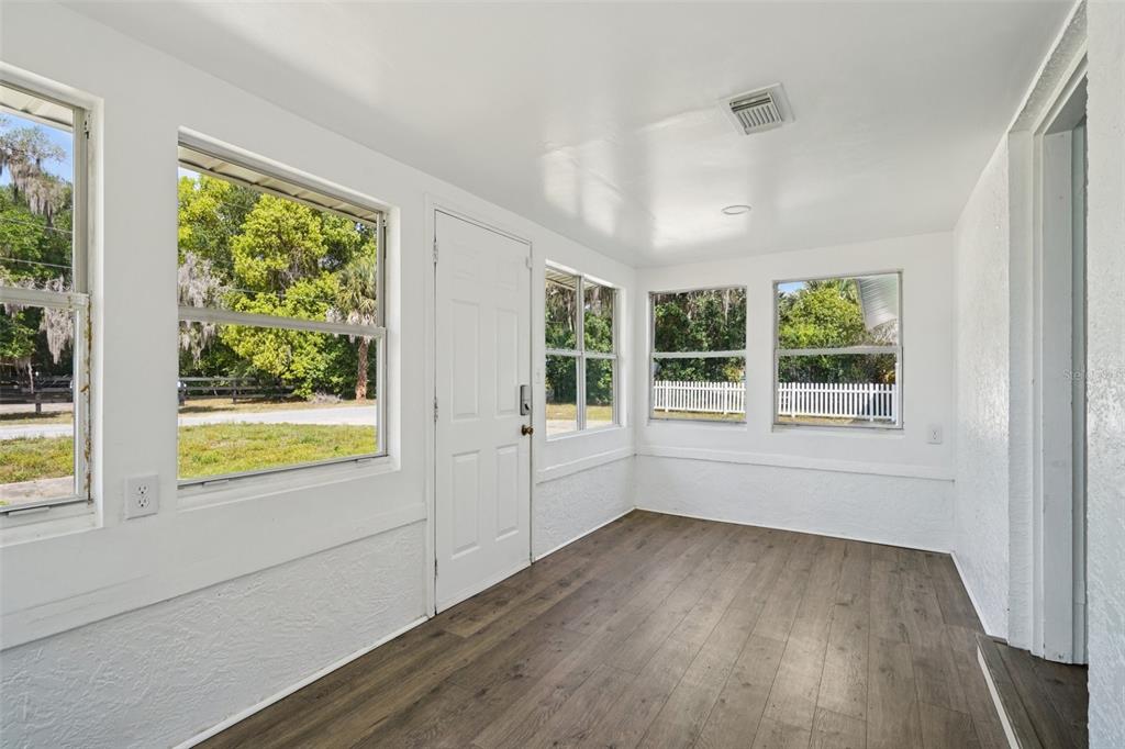 A sunroom with white walls, wood-look flooring, multiple windows, and a white entry door — 12385 SE 135TH COURT, OCKLAWAHA, FL