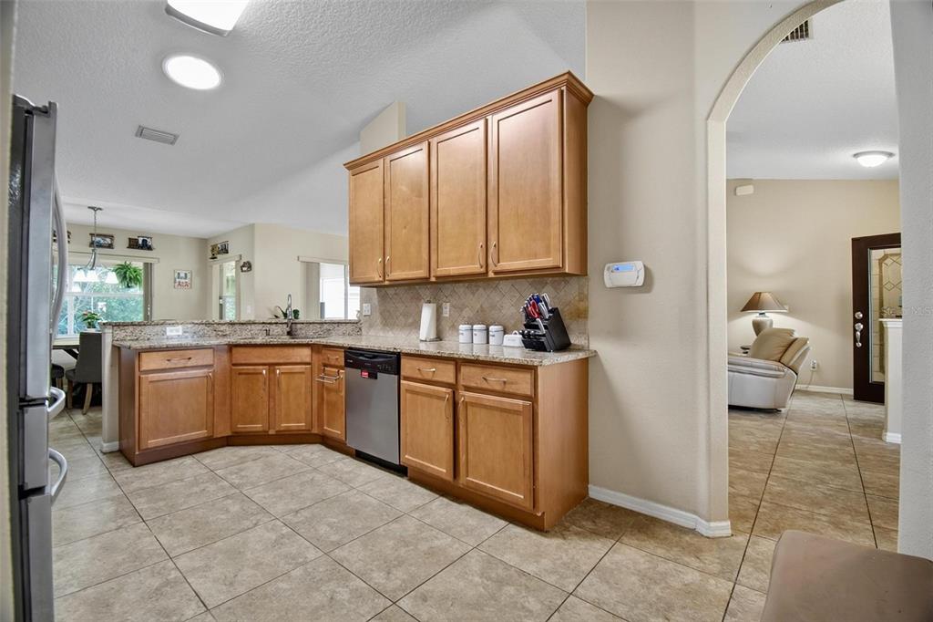 A kitchen features light wood cabinets, granite countertops, a stainless steel dishwasher, and tile flooring — 203 FRONTIER DRIVE, PALM COAST, FL