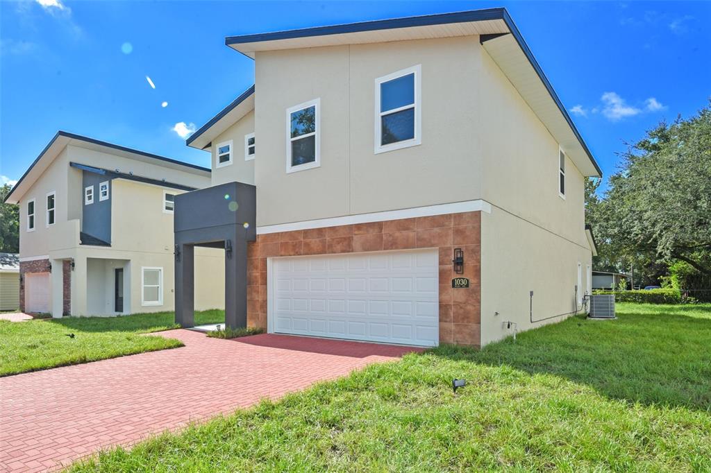 A two-story house with a tan stucco exterior, a brick-tiled garage base, and a red driveway — 1030 WILKS AVENUE, ORLANDO, FL