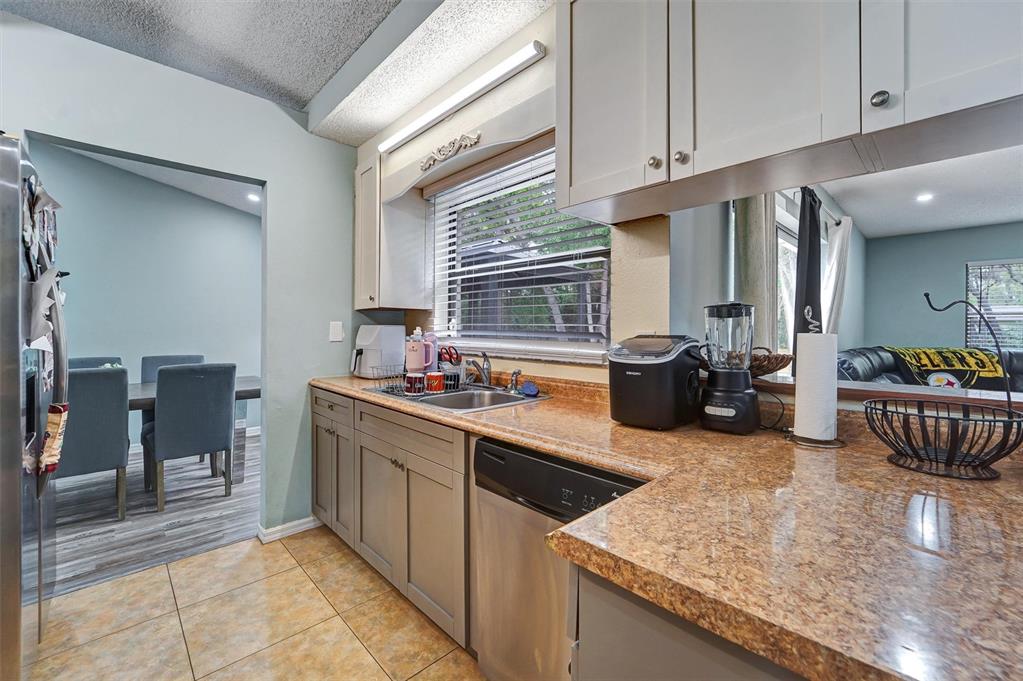 A kitchen features granite countertops, gray cabinets, stainless steel appliances, and a view into the dining area — 1250 FINLAND DRIVE, SPRING HILL, FL