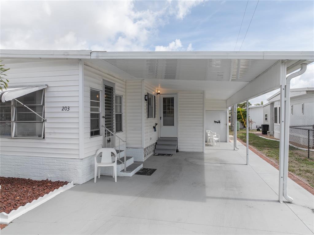 A white mobile home exterior features a covered carport, concrete driveway, and front entrance steps — 203 HARVEST LANE, NORTH FORT MYERS, FL