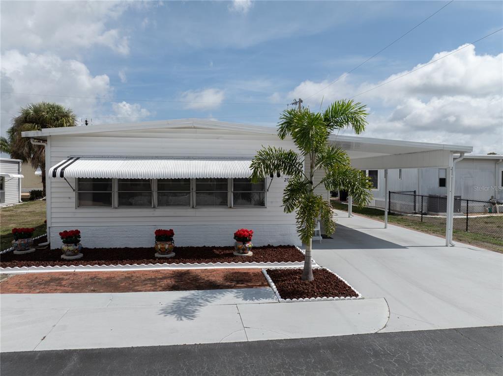 A white mobile home with a carport, an awning, and a small landscaped front yard — 203 HARVEST LANE, NORTH FORT MYERS, FL