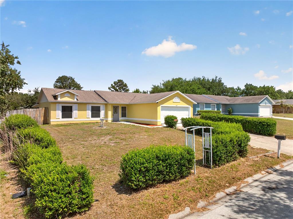 A yellow single-story house with a white garage and a manicured hedge-lined front yard — 10810 CRESCENDO LOOP, CLERMONT, FL