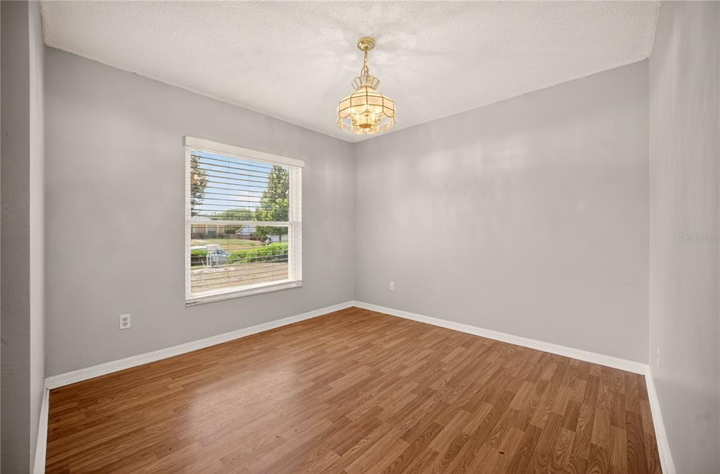 An empty room with light gray walls, wood-look flooring, a window, and a hanging chandelier — 10810 CRESCENDO LOOP, CLERMONT, FL