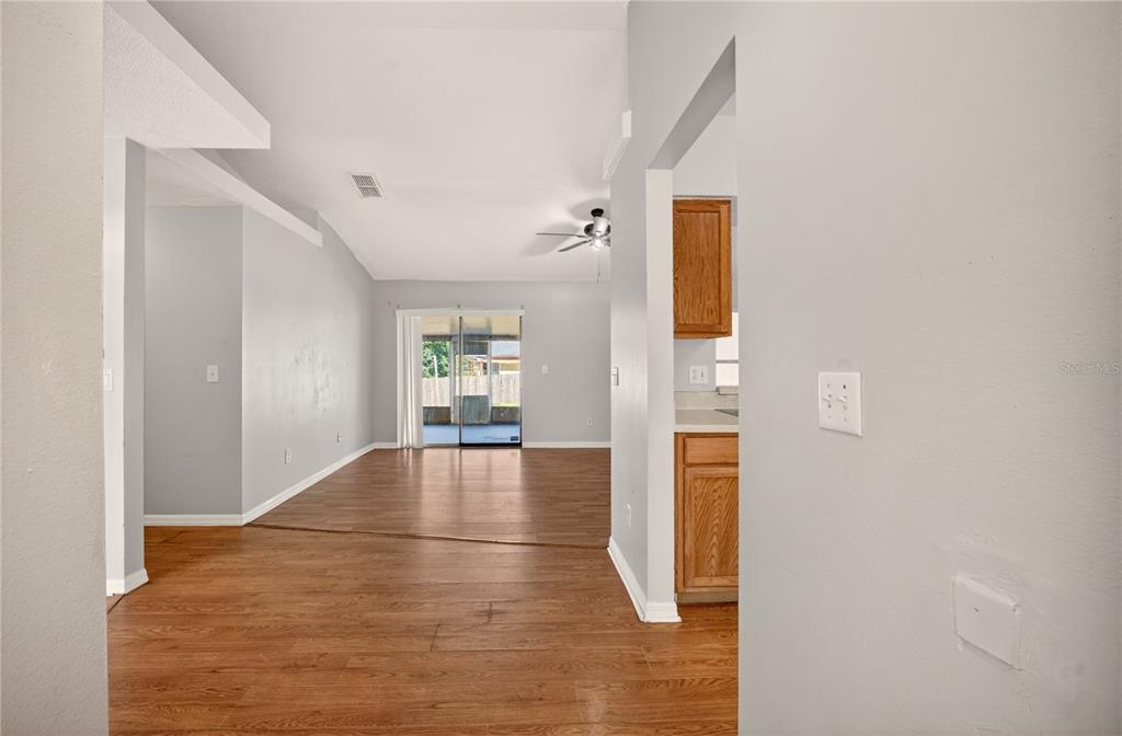 A view from a hallway looking into a living area with wood-look flooring and sliding doors — 10810 CRESCENDO LOOP, CLERMONT, FL