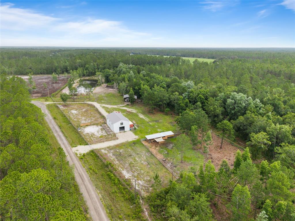 An aerial view shows a white barn, a small pond, and fenced pastures amidst woods — 5747 RETREAT ROAD, KEYSTONE HEIGHTS, FL