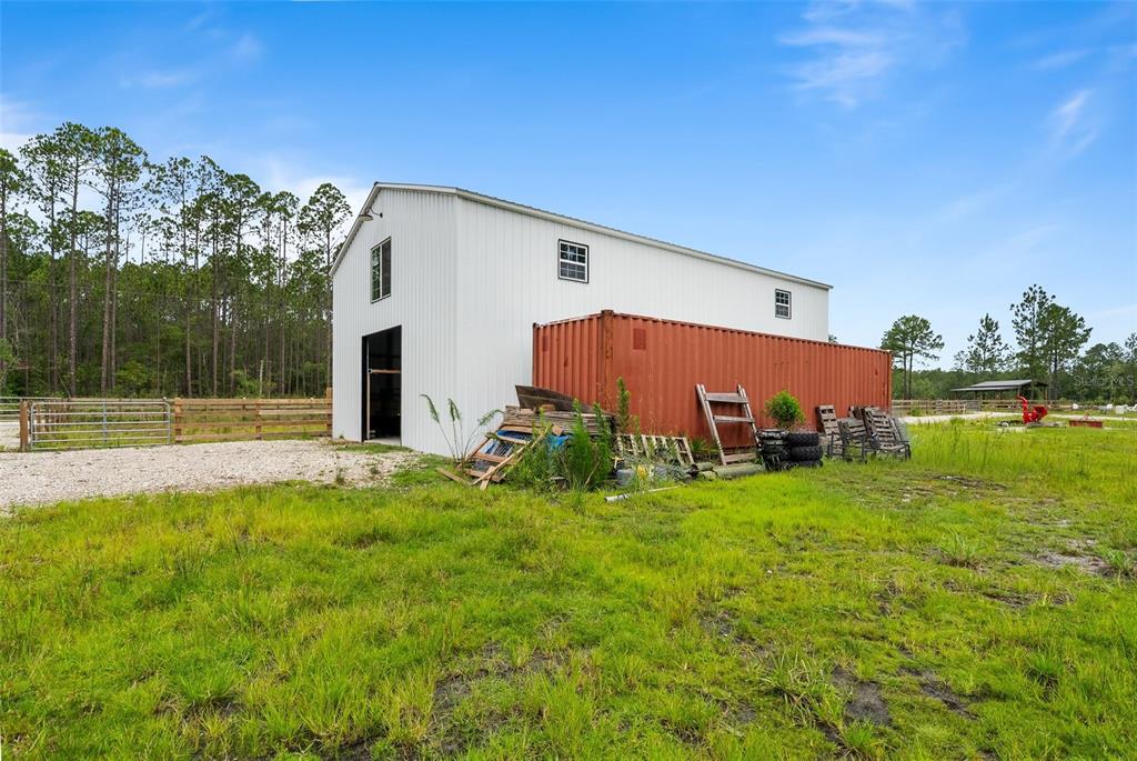 A white metal barn with an attached red shipping container sits on a grassy lot — 5747 RETREAT ROAD, KEYSTONE HEIGHTS, FL