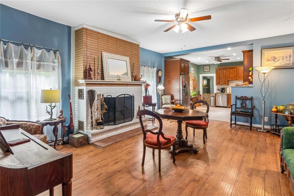 A living room with a brick fireplace, wood flooring, and an open view into the kitchen — 6202 STAFFORD ROAD, PLANT CITY, FL