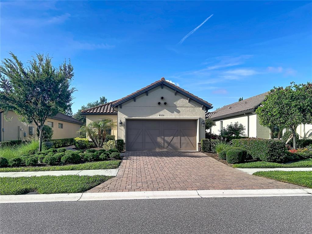 A single-story house with a beige stucco exterior, a brown garage door, and a brick driveway — 8335 ALBERATA VISTA DRIVE, TAMPA, FL