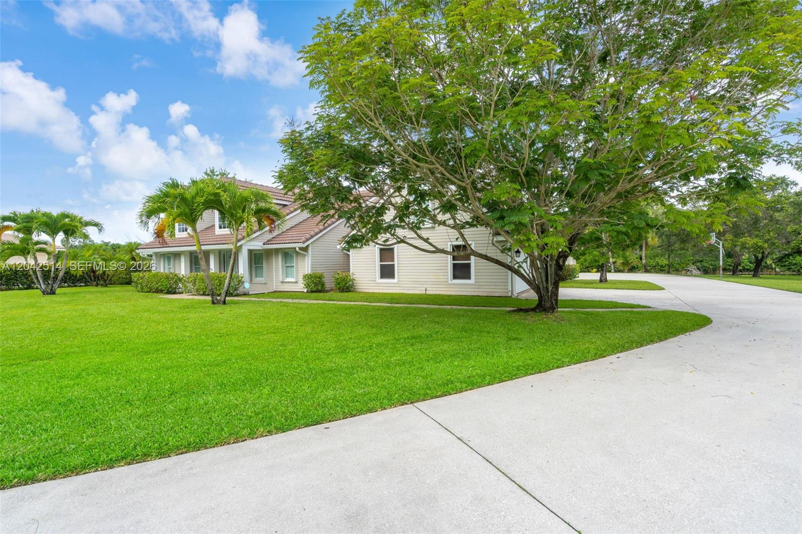 A beige house with a large tree and a concrete driveway under a blue sky — 5703 Lago Del Sol Dr, Lake Worth FL 33449, LAKE WORTH, FL