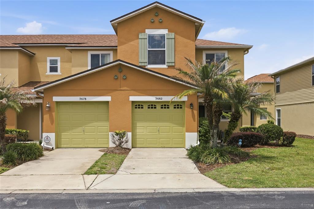 The exterior of a two-story townhouse with two light green garage doors and tan stucco — 3682 SOARING LANE, SANFORD, FL