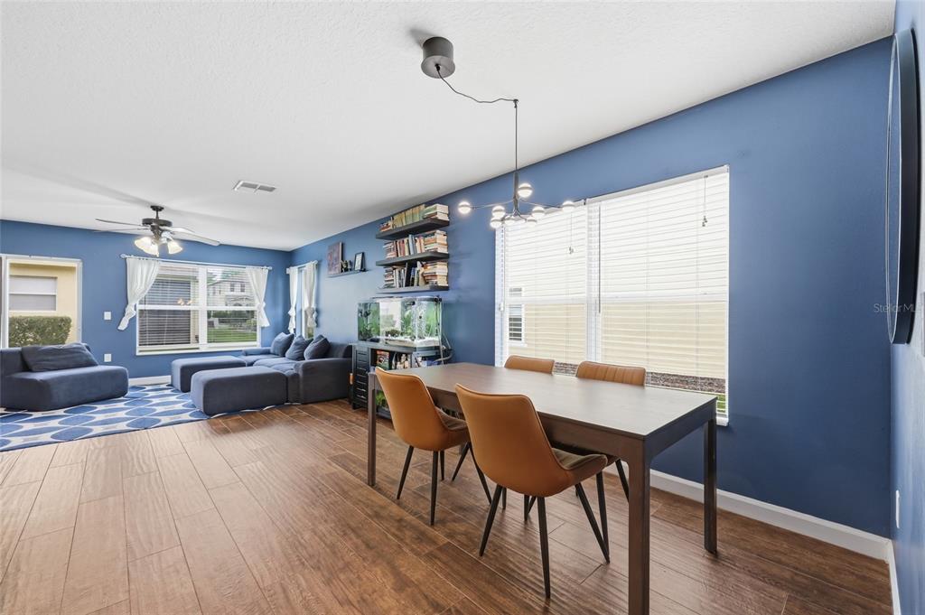 A dining area and living room with blue walls, wood-look flooring, and a modern chandelier — 3682 SOARING LANE, SANFORD, FL