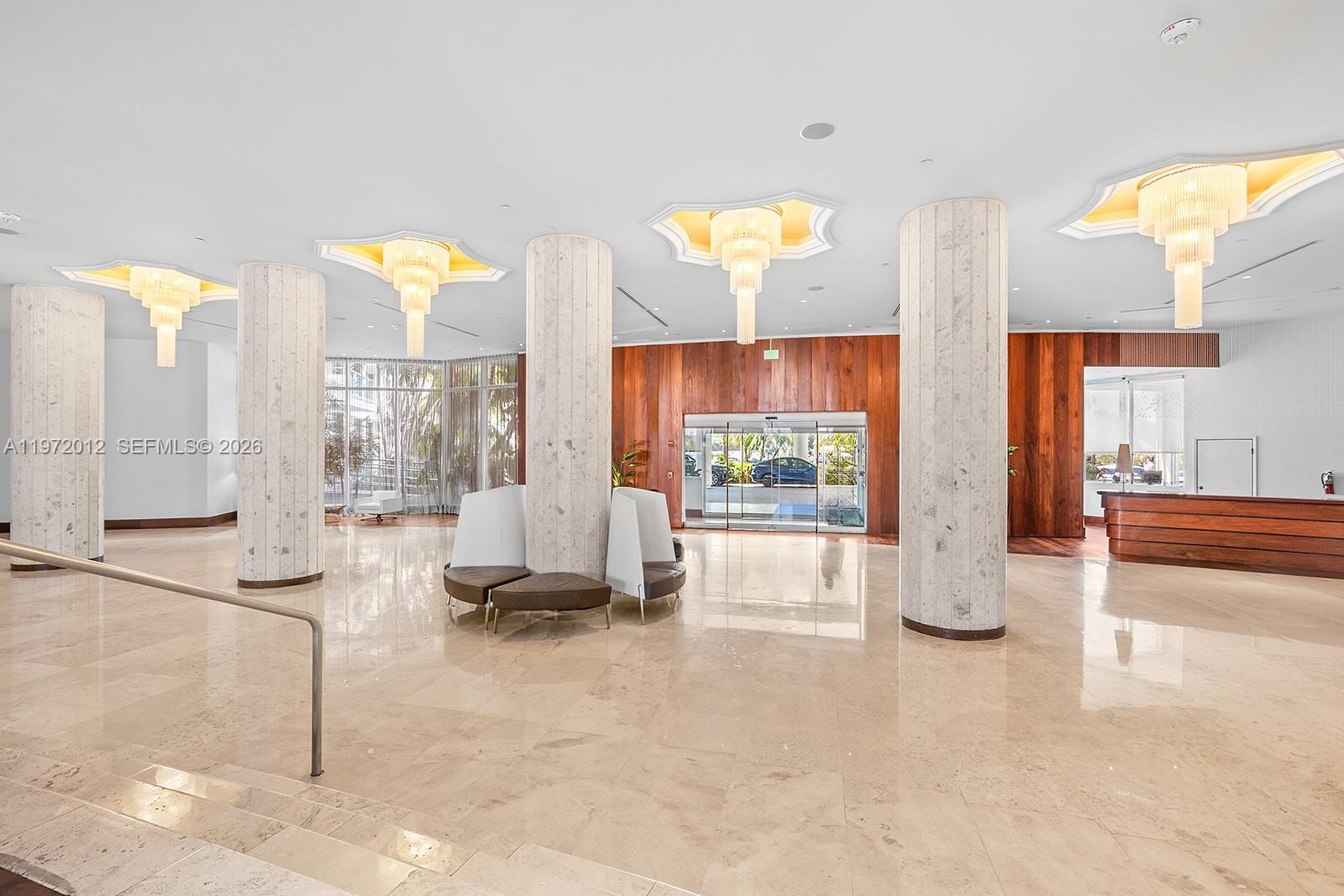 A spacious lobby features marble floors, large cylindrical columns, wood paneling, and tiered chandeliers — 5161 Collins Ave # 910, Miami Beach FL 33140, MIAMI BEACH, FL