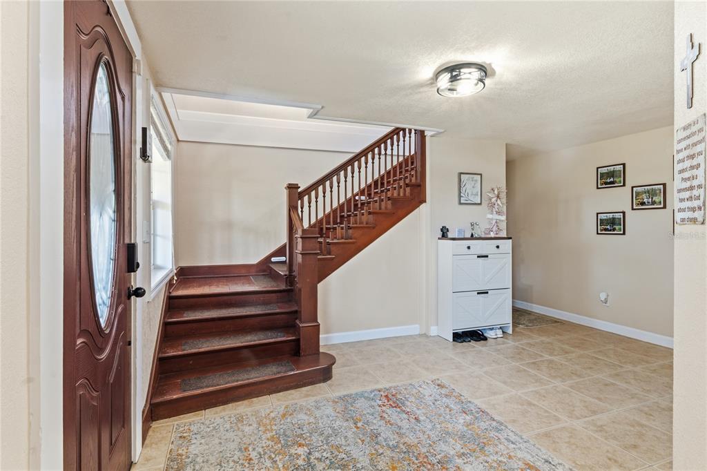 An entryway features a wooden staircase, tile flooring, a white shoe cabinet, and a front door — 1660 E MAIN STREET, BARTOW, FL