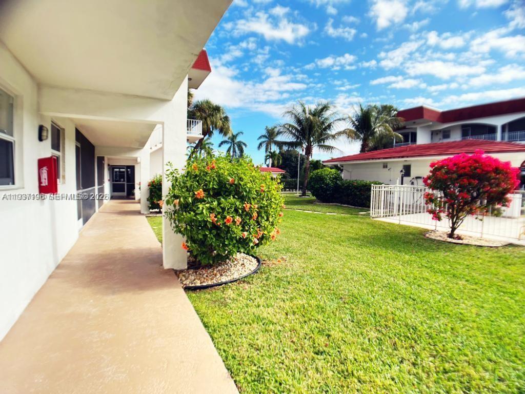 A covered walkway leads past a flowering bush toward a building with a lawn — 580 Egret Dr # 302, Hallandale Beach FL 33009, HALLANDALE BEACH, FL