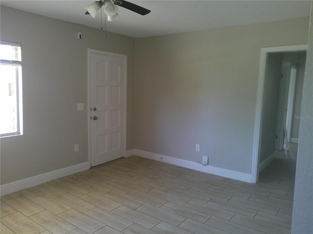 An empty room features light-colored tile flooring, gray walls, a white door, and a ceiling fan — 1241 NICHOLSON STREET, CLEARWATER, FL