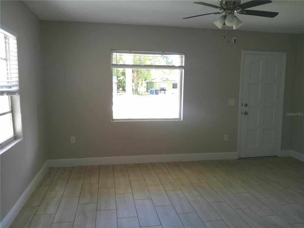 An empty room features light-colored wood-look tile flooring, gray walls, a ceiling fan, and windows — 1241 NICHOLSON STREET, CLEARWATER, FL