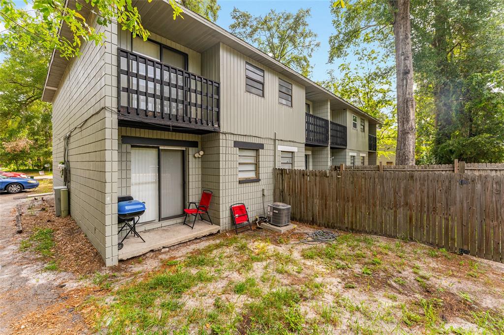A two-story apartment building exterior with a small concrete patio, wooden fence, and balcony — 724 SW 68TH TERRACE, GAINESVILLE, FL