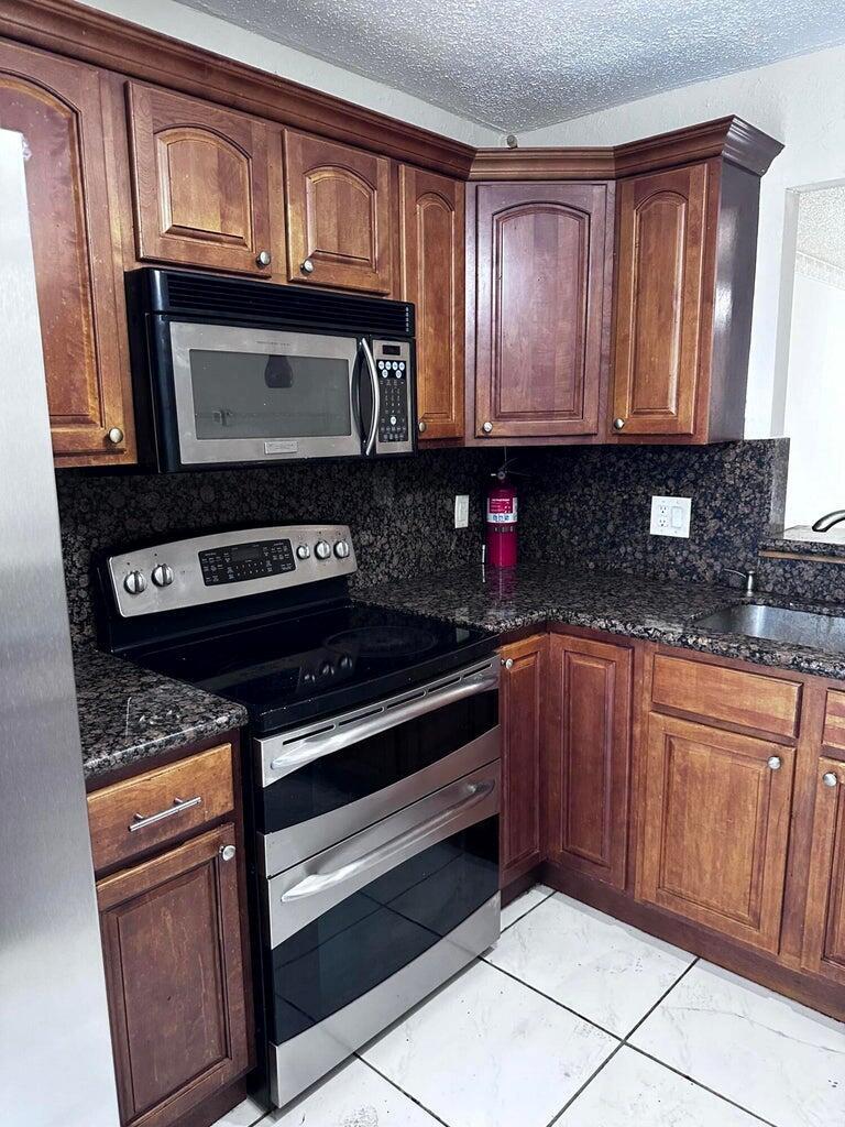 A kitchen features wood cabinets, stainless steel appliances, and dark granite countertops — 6200 S Falls Cir Drive # 310, Lauderhill FL 33319, LAUDERHILL, FL
