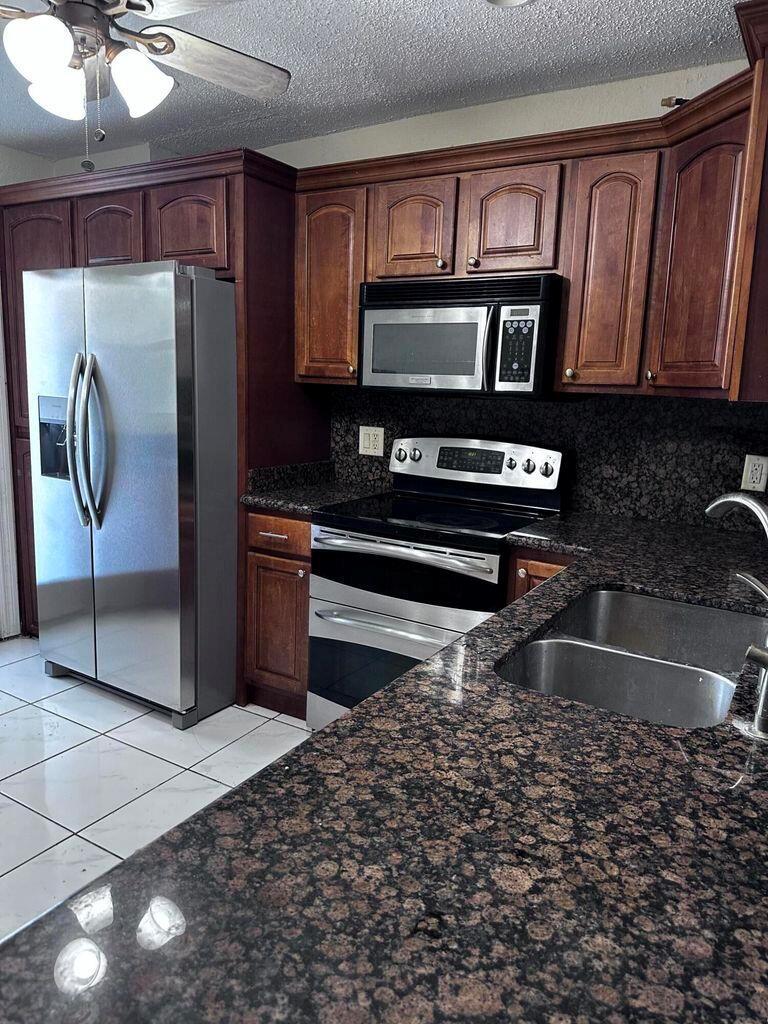 A kitchen features dark wood cabinets, granite countertops, stainless steel appliances, and white tile flooring — 6200 S Falls Cir Drive # 310, Lauderhill FL 33319, LAUDERHILL, FL