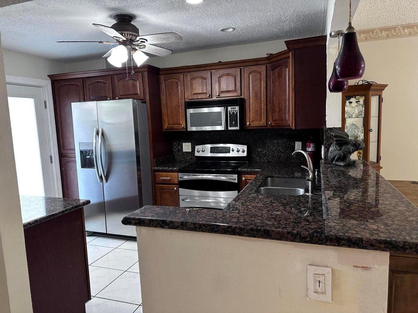 A kitchen features dark wood cabinets, granite countertops, stainless steel appliances, and a ceiling fan — 6200 S Falls Cir Drive # 310, Lauderhill FL 33319, LAUDERHILL, FL