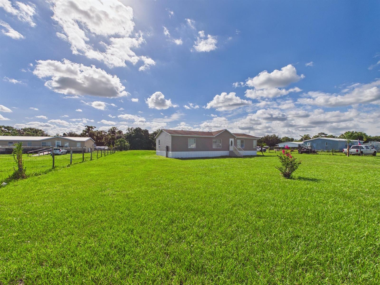 A tan manufactured home sits in the center of a large, grassy, fenced-in lot — 17090 NW 38th Avenue, Okeechobee FL 34972, OKEECHOBEE, FL
