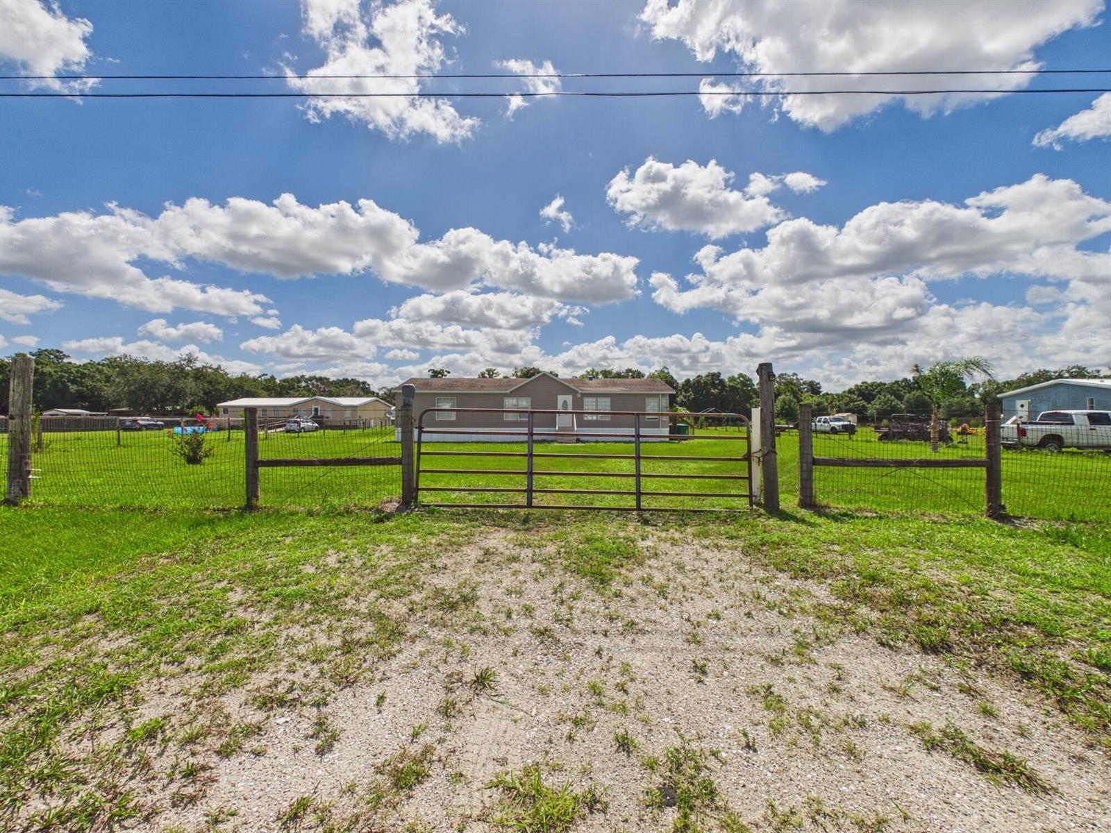 A single-story house sits behind a metal gate and wire fence on a grassy lot — 17090 NW 38th Avenue, Okeechobee FL 34972, OKEECHOBEE, FL