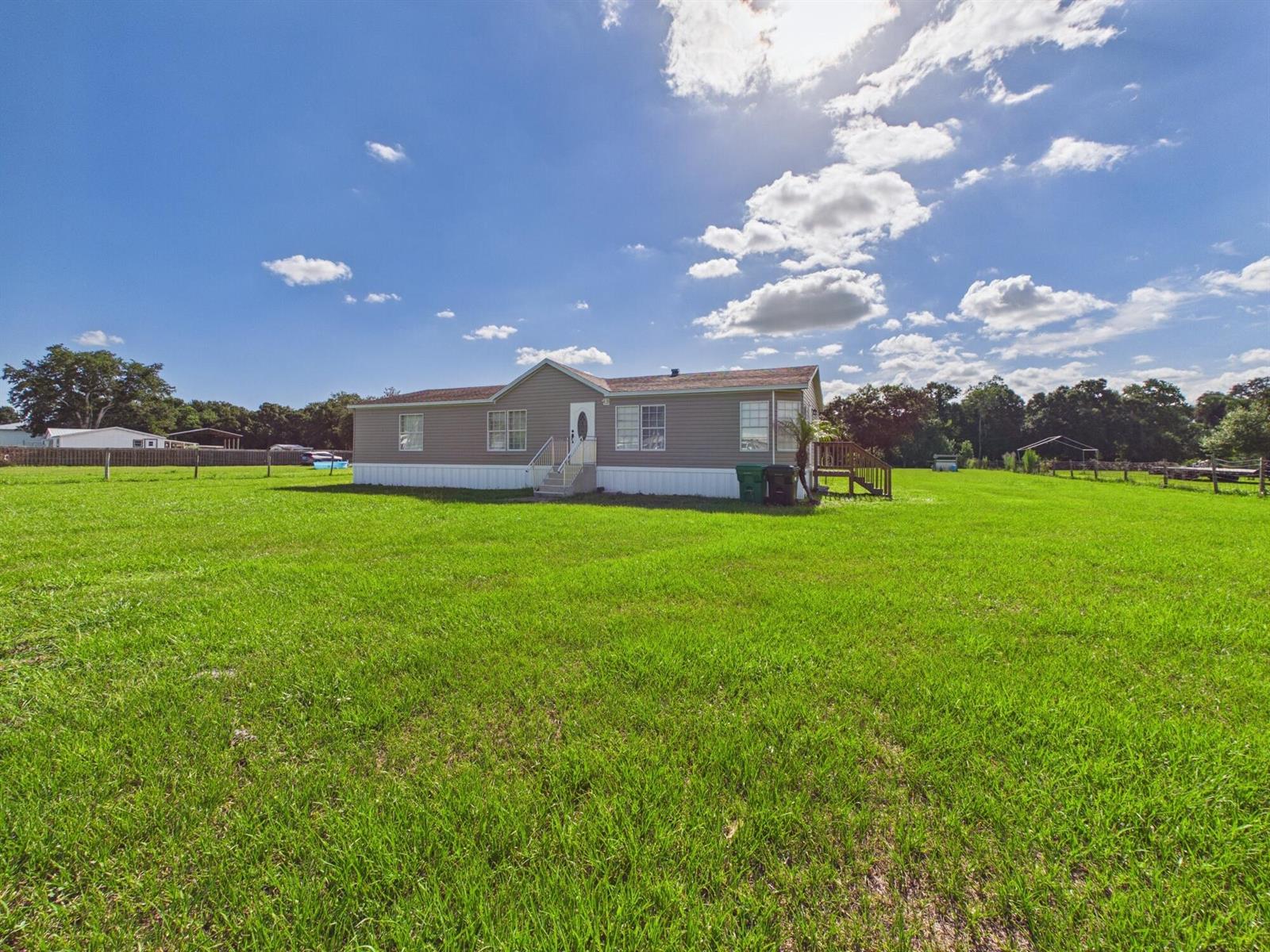 A single-story manufactured home sits in the middle of a large, grassy field — 17090 NW 38th Avenue, Okeechobee FL 34972, OKEECHOBEE, FL