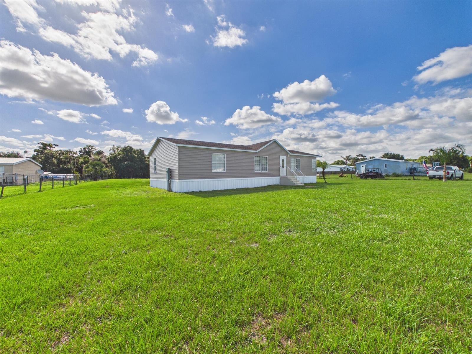 A tan manufactured home sits on a large, grassy lot under a blue sky — 17090 NW 38th Avenue, Okeechobee FL 34972, OKEECHOBEE, FL