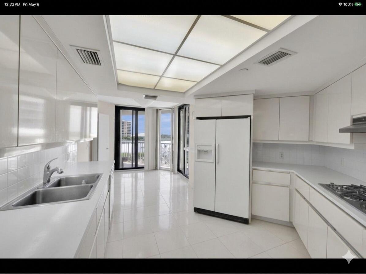 A white modern kitchen features glossy cabinets, tile flooring, and a view of the water — 3170 S Ocean Boulevard # 201n, Palm Beach FL 33480, PALM BEACH, FL