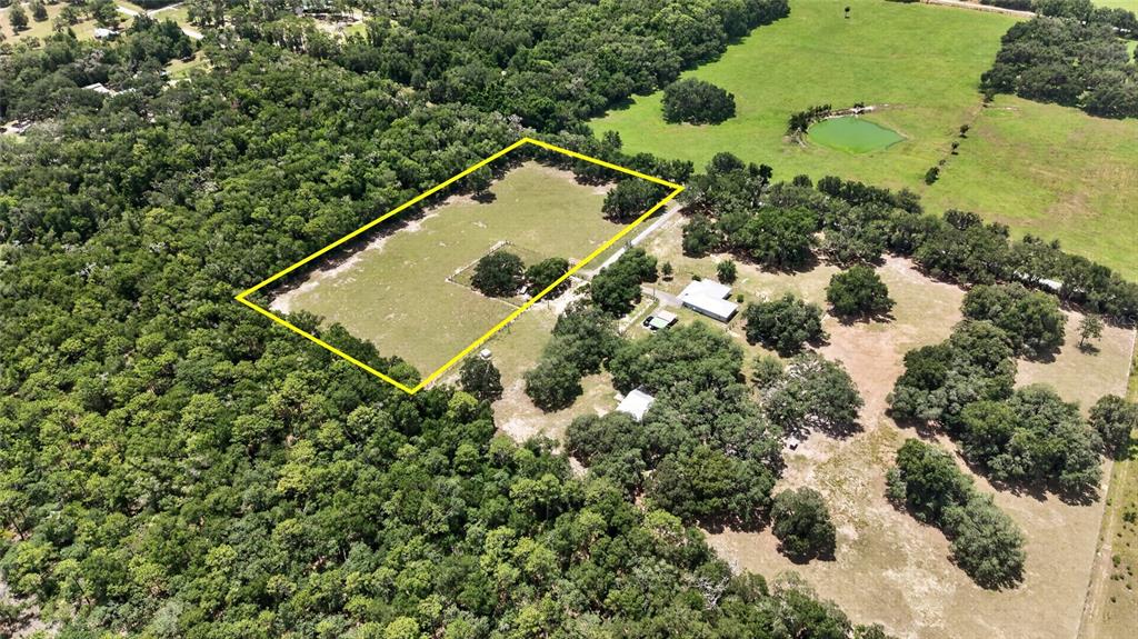 An aerial view shows a rectangular fenced pasture surrounded by dense trees and rural buildings — 2741 E STAGE COACH TRAIL, INVERNESS, FL