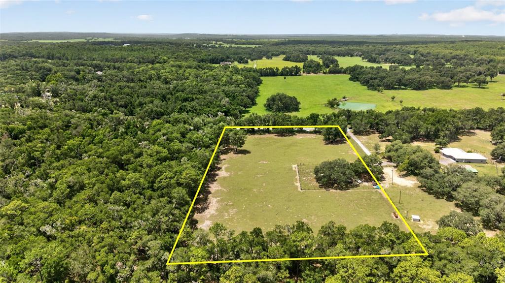 An aerial view shows a rectangular fenced pasture surrounded by dense forest and nearby buildings — 2741 E STAGE COACH TRAIL, INVERNESS, FL