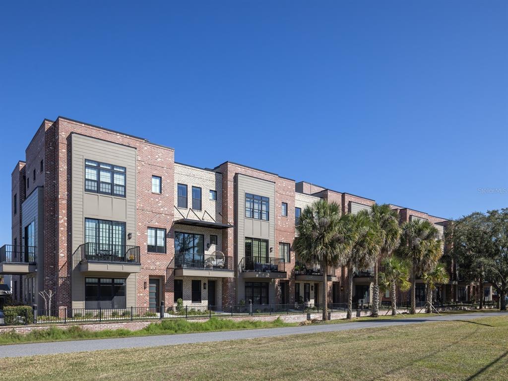 A multi-story brick and tan apartment building features balconies and large windows under a clear sky — 64 N PARK AVENUE, WINTER GARDEN, FL