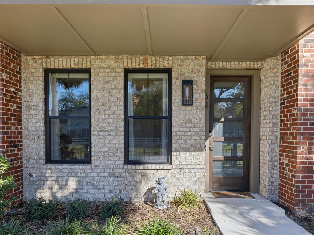 A brick house exterior features two black-framed windows, a wooden front door, and landscaping — 64 N PARK AVENUE, WINTER GARDEN, FL