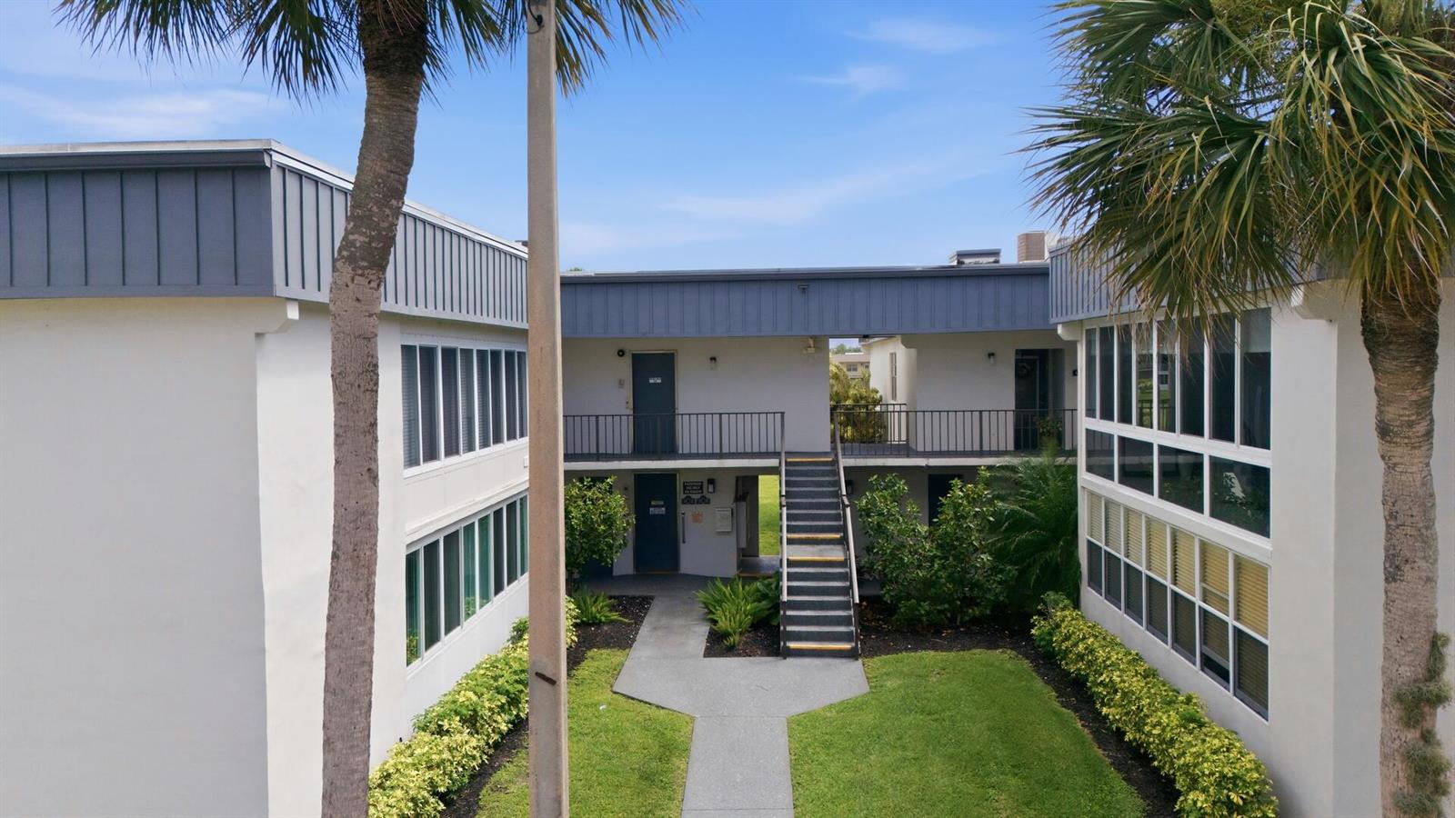 An exterior view of a two-story apartment building with a central courtyard and staircase — 563 Piedmont L, Delray Beach FL 33484, DELRAY BEACH, FL
