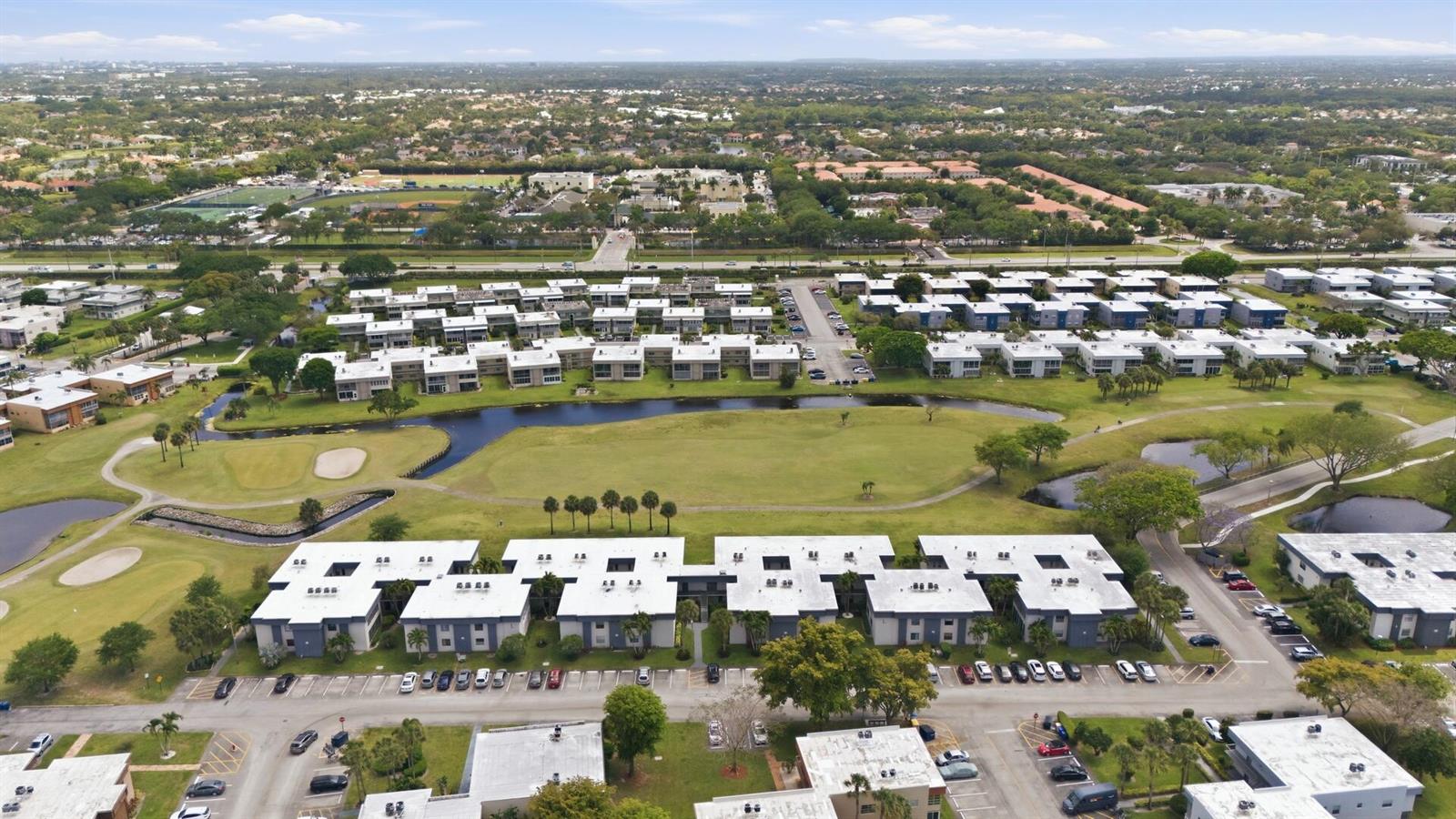 An aerial view of a residential complex with flat-roofed buildings, a golf course, and parking — 563 Piedmont L, Delray Beach FL 33484, DELRAY BEACH, FL