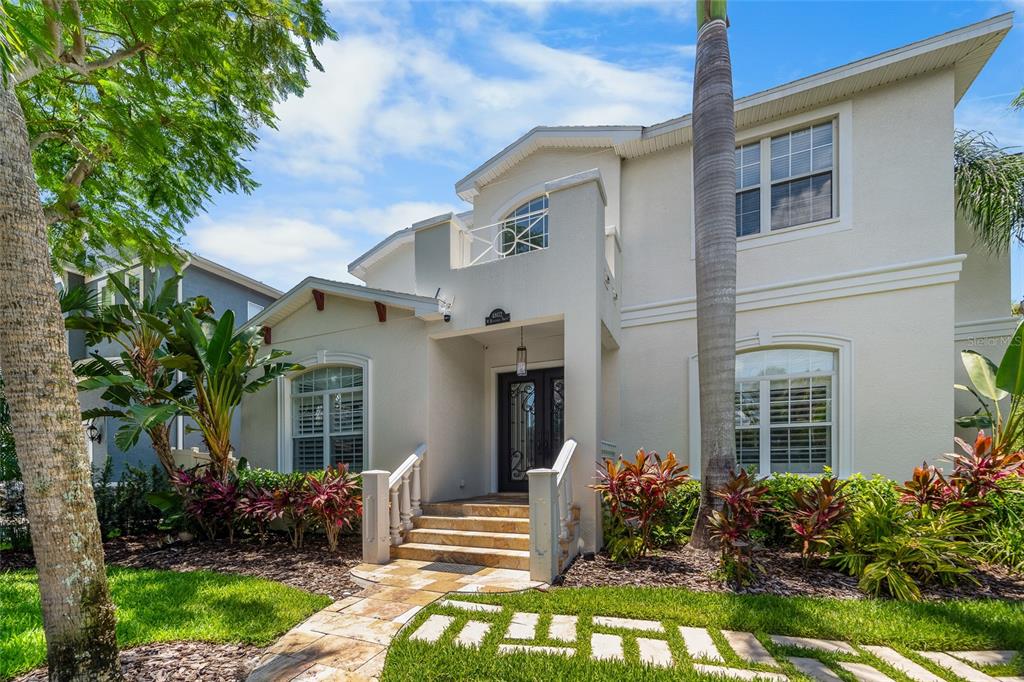 A two-story house with a beige stucco exterior, a front porch, and tropical landscaping — 4802 W BEACHWAY DRIVE, TAMPA, FL