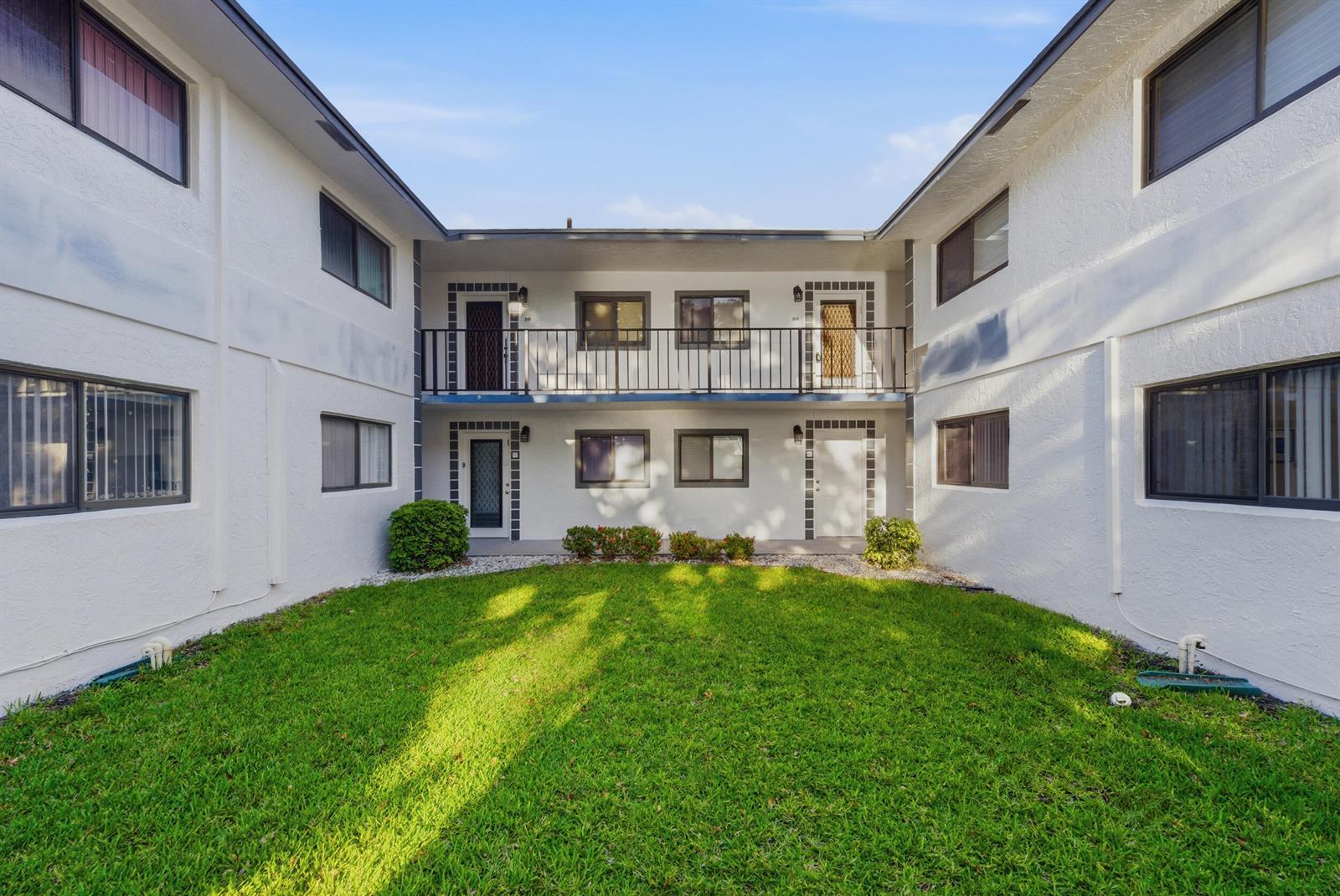 A two-story apartment building exterior features a central courtyard with a lawn and balcony — 15301 Pembridge Avenue # 44, Delray Beach FL 33484, DELRAY BEACH, FL