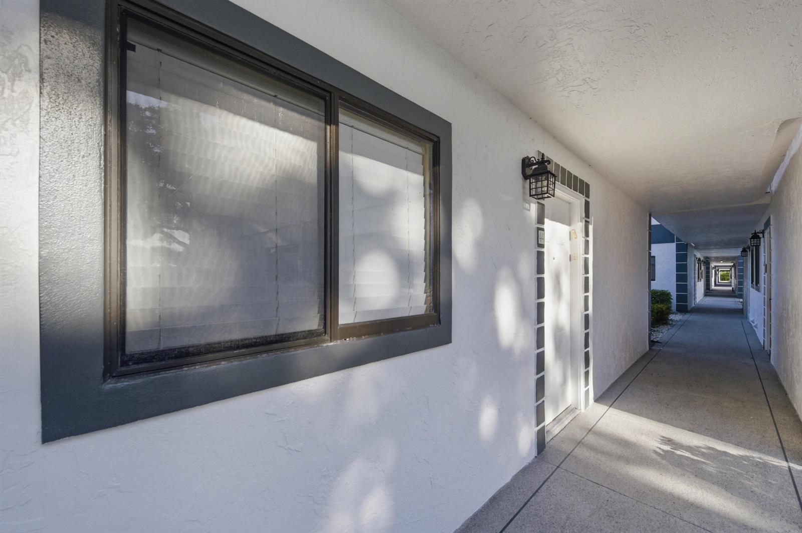 An exterior view of a white building with a window and a door along a walkway — 15301 Pembridge Avenue # 44, Delray Beach FL 33484, DELRAY BEACH, FL