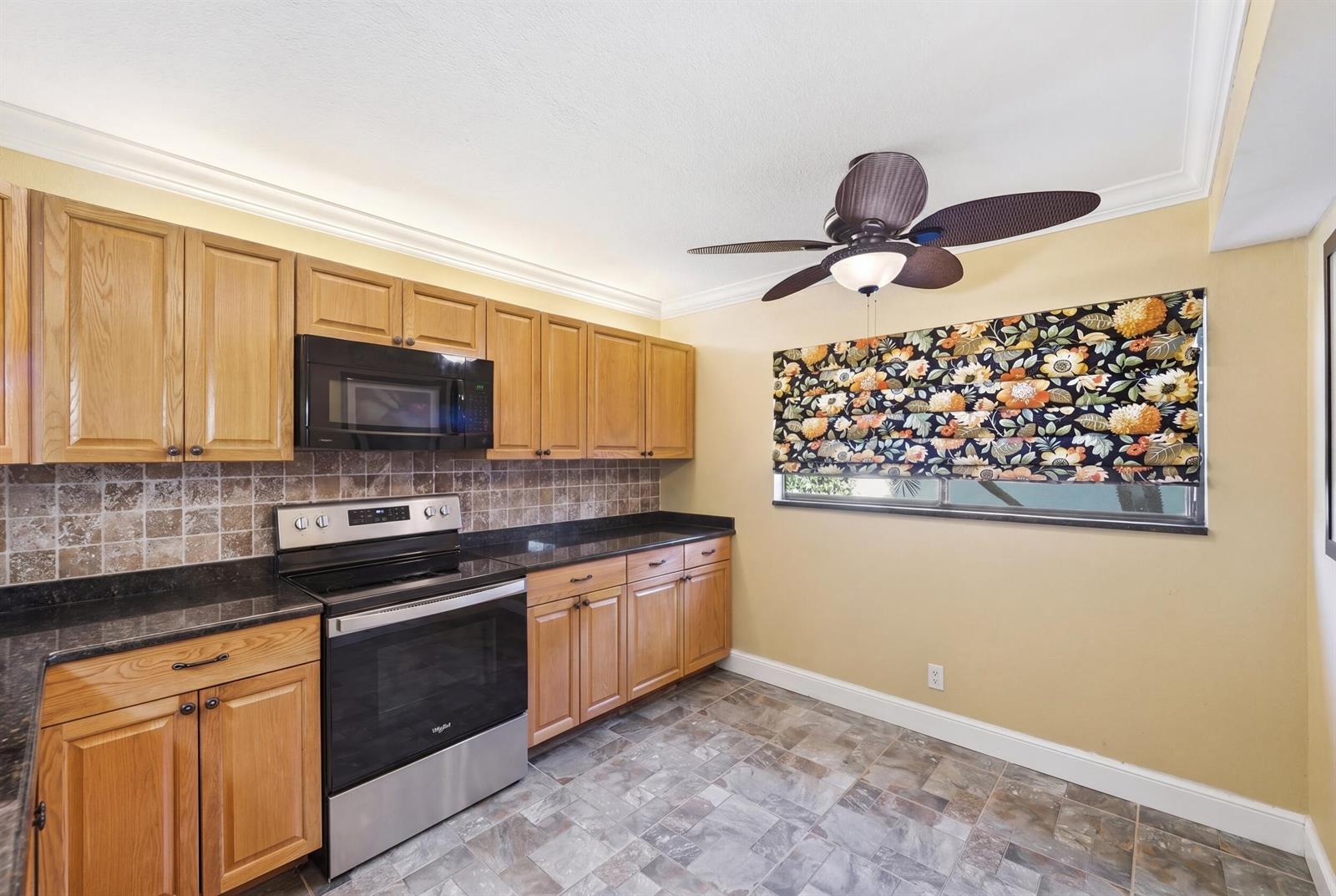 A kitchen features oak cabinets, black countertops, stainless steel appliances, and a patterned window shade — 15301 Pembridge Avenue # 44, Delray Beach FL 33484, DELRAY BEACH, FL
